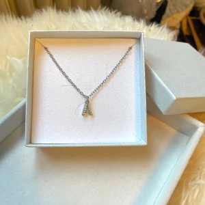 Silverhalsband med bokstav A och stenar - Snyggt halsband i silverfärg & rostfritt stål med ett hänge i form av bokstaven A, dekorerat med små glittrande stenar. Kedjan är tunn och stilren, perfekt för att ge en personlig touch till din look.