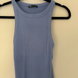 Ljusblå ribbad långklänning från Zara - Säljer en ljusblå ribbad långklänning från Zara. Klänningen är ärmlös med rund halsringning och har en tight passform. Perfekt för dig som gillar en enkel och stilren look. Materialet är mjukt och stretchigt, vilket gör den superbekväm att bära.