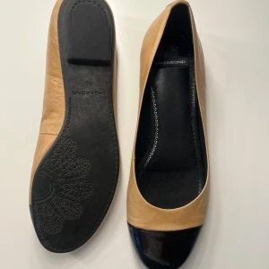 Ballerinaskor  - Snygga ballerinaskor från Vagabond i beige skinn med svart, glansig tå. Skorna har rund tå och platt sula, perfekt för en stilren look. Klassisk design med diskret logga på innersulan.