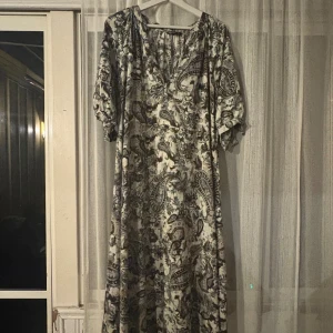 Mönstrad långklänning från SHEIN Curve - Långklänning från SHEIN Curve med v-ringning och korta ärmar. Klänningen har ett paisleyinspirerat mönster i blått, grått och beige på vit botten. Luftig passform och perfekt för dig som gillar bohemisk stil.