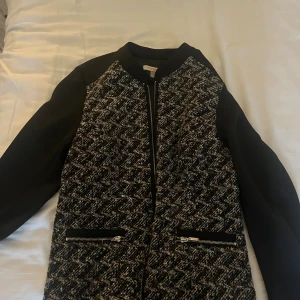 Svart och grå bomberjacka från Notex - Snygg bomberjacka från Notex med svart bas och gråmelerat, rutig mönster framtill. Jackan har långa ärmar, dragkedja framtill och två fickor med coola dragkedjor. Perfekt för dig som gillar en stilren men ändå unik look.