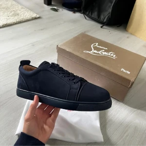 Mörkblå sneakers från Christian Louboutin - Snygga mörkblå sneakers från Christian Louboutin i mocka med klassisk röd sula och diskret logga. Skorna har rund tå, platt sula och snörning. Insidan är fodrad i beige läder för extra komfort. Perfekta för dig som vill ha en stilren och lyxig look.
