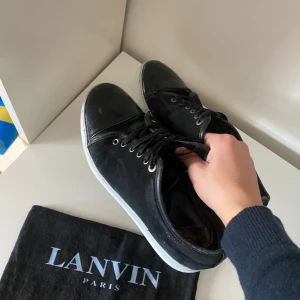 Svarta Lanvin skor - Snygga svarta sneakers från Lanvin Paris med ovandel i mocka och tå i blankt skinn. Skorna har vita sulor, svarta snören och metallfärgade öljetter. Klassisk och stilren design som passar till det mesta. Dustbag från Lanvin medföljer. Skorna är i 7/10 i skicket. Priset är inte hugget i sten, hör av dig vid frågor.