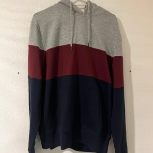 Färgglad hoodie med huva och ficka - Snygg hoodie i blockfärger med grått upptill, vinrött i mitten och mörkblått nedtill. Tröjan har huva med snörning och en stor magficka. Perfekt för dig som gillar en avslappnad och cool stil.