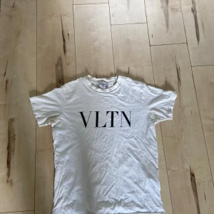 Vit VLTN t-shirt från Valentino - Snygg vit t-shirt från Valentino med stor VLTN-print på bröstet. Klassisk rund hals och korta ärmar. Tillverkad i mjuk bomull som känns skön mot huden. Perfekt för dig som gillar stilrena designer och exklusiva märken.