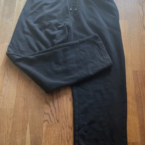 Svart mjukisbyxor - Svarta mjukisbyxor i bomull med elastisk midja och dragsko. Byxorna har en avslappnad passform och raka ben, perfekta för chill dagar eller när du vill vara bekväm. En bakficka och mjukt material gör dem extra sköna.