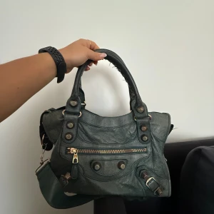 ÄKTA Balenciaga grön handväska i skinn - Cool grön handväska från Balenciaga i mjukt skinn med snygga detaljer som guldiga dragkedjor, nitar och spännen. Väskan har både handtag och axelrem, spegel! Skriv om du har fler frågor! Jättebra skick både utanpå och inuti❤️