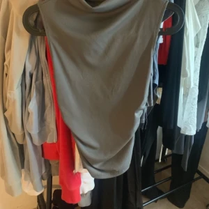 Grå ärmlös topp med drapering - Snygg grå topp med ärmlös design och draperad halsringning. Toppen har en enkel, stilren look och är tillverkad i ett mjukt, stretchigt material som sitter skönt på kroppen. Perfekt för dig som gillar minimalistisk stil.