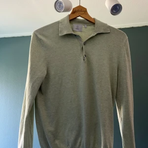 Ljus grön pikétröja från Bläck - Snygg ljusgrå pikétröja från Bläck med klassisk krage och knappar framtill. Tröjan har lång ärm och är tillverkad i mjukt material som känns skönt mot huden. Perfekt för dig som gillar stilrena och enkla plagg.