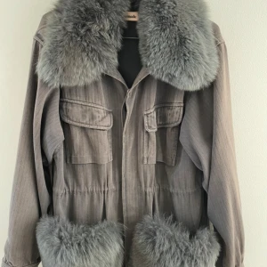 Grå pälsjacka Windie Custommade S-M - Snygg grå jacka från Custommade med fluffig rävpäls vid krage och fickor. Jackan är i mycket bra skick och i storlek S-M. 