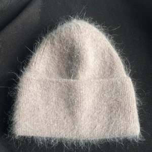 Beige fluffig mössa i kashmir - Supermjuk och fluffig beige mössa i kashmir med enkel, klassisk form och uppvikt kant. Perfekt för dig som vill ha en stilren look med extra mysfaktor. Mössan har en ljus ton och känns lyxig tack vare det exklusiva materialet. Oanvänd 