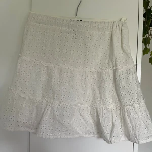 Vit kort volangkjol - Superfin vit kortkjol från i storlek XXS. Kjolen har broderade hålmönster, volanger och resår i midjan. Perfekt för dig som gillar romantisk och söt stil. Tillverkad i bomull för en luftig känsla.