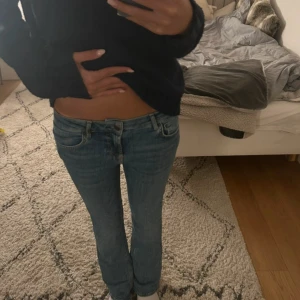 Blå bootcut jeans med låg midja - Snygga blå jeans med låg midja och klassisk bootcut-passform. Jeansen har fem fickor, bälteshällor och dragkedja med knapp framtill. Perfekta för en avslappnad och trendig look.