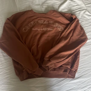 Brun sweatshirt från Lindex med text - Säljer en brun sweatshirt från Lindex med broderad text 'ONE OF A KIND making a difference' på bröstet. Tröjan har rund hals, ribbade muddar och är långärmad. Perfekt för dig som gillar chill och enkel stil.