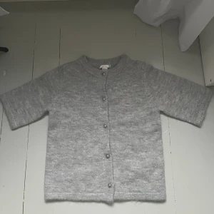 Grå kofta från Gina Tricot Young - Grå kofta från Gina Tricot Young. Koftan har rund hals, kortare ärmar och pärlknappar framtill. Aldrig använd, skriv privat vid frågor. 