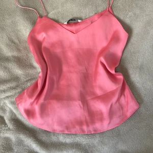 Rosa linnetopp från Stradivarius - Säljer en snygg rosa linnetopp från Stradivarius i storlek S. Toppen har tunna axelband, v-ringning och är tillverkad i ett glansigt, mjukt material som ger en lyxig känsla. Perfekt för varma dagar eller när du vill ha en enkel men stilren look.