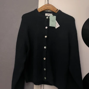 Mörkblå stickad kofta från Gina Tricot - Mysig mörkblå stickad kofta från Gina Tricot i ullblandning. Koftan har rund halsringning, långa ärmar och knäpps med pärlemorskimrande knappar framtill. Perfekt för lager-på-lager och enkel att styla till olika looks.