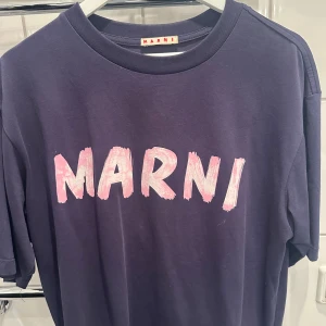 Lila Marni t-shirt med tryck - Snygg lila t-shirt från Marni med stort rosa logotyp-tryck framtill. Klassisk rund halsringning och korta ärmar. Tillverkad i mjuk bomull för en skön känsla. Perfekt för dig som vill sticka ut med en cool statement-tee.