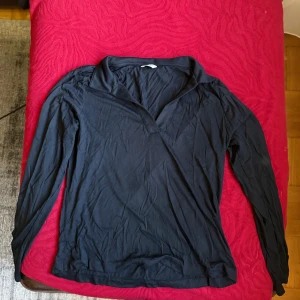 Svart långärmad tröja med krage - Svart långärmad tröja med snygg krage och v-ringad hals. Enkel och stilren modell som passar perfekt till jeans eller kjol. Mjuk och skön känsla, perfekt för lager-på-lager under kyligare dagar.