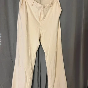 Beiga kostymbyxor från Lindex M - Stilrena beiga kostymbyxor från Iindex i storlek M. Byxorna har raka ben, klassisk midja och stängs med knapp och dragkedja. Perfekta för en clean och snygg look. Materialet känns mjukt och lätt, vilket gör dem bekväma hela dagen.