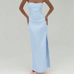 Ljusblå axelbandslös långklänning - Supersnygg ljusblå långklänning med axelbandslös design och hög slits på sidan. Klänningen har en figurnära passform och draperad midja som framhäver siluetten. Säljer billigt då kvaliteten inte uppfyller det jag förväntade mig! Skickar gärna passform samt mer bilder om du är intresserad! Vid snabb affär kan jag gå ner i pris! 