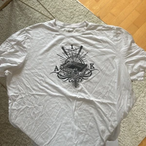 Vit AIK t-shirt från Nike - Vit t-shirt från Nike med AIK-tryck på bröstet och svart Nike-logga på ärmen. På ryggen står det 'AFFE' i svart text. Klassisk passform och rund halsringning, tillverkad i mjuk bomull. Storlek xl 