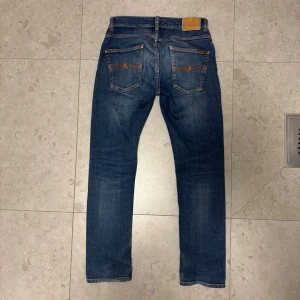 Blå Jeans från Nudie Jeans - Snygga blå jeans från Nudie Jeans med klassisk femficksdesign i modellen Grim Tim. Jeansen har en slim/rak passform och är tillverkade i slitstarkt denim med lätt tvättad look. Säljer pga att de inte passar mig längre. Strlk 30/30, tveka inte på att höra av dig vid frågor!