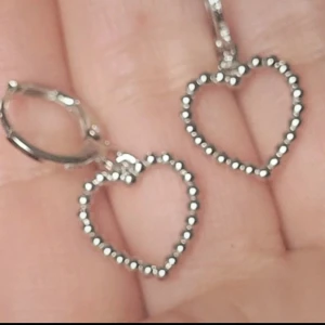  Helt nya Silverfärgade hjärtörhängen -  Säljer  helt nya ett par söta örhängen i silverfärg med hjärtformade hängen. Hjärtana är dekorerade med små kulor längs hela kanten vilket ger en unik och trendig look. Perfekta för att ge din outfit en romantisk touch.