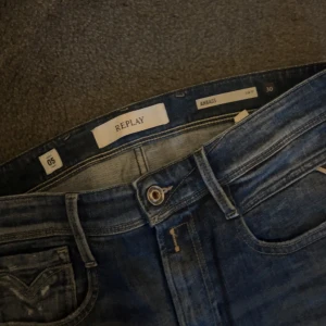 Replay jeans med slitningar - Snygga blå Replay Anbass jeans med slitna detaljer och tvättad look. Klassisk femficksmodell med dragkedjegylf och logga på fickan. Jeansen har en rak passform och är tillverkade i mjukt denimtyg som sitter skönt hela dagen.