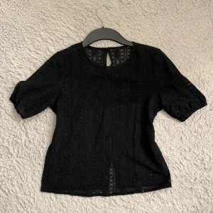 Svart spetsblus med knappar - Säljer denna söta blus i spets med korta ärmar och rund halsringning. Blusen har fina spetsdetaljer och knäppning med små svarta knappar längs ryggen. Har endast använts 1 gång🩷
