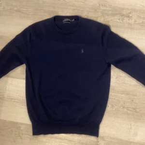 Stickad Ralph Lauren tröja - Marin blå stickad tröja från Ralph lauren i storlek S, jätte skönt material och sitter extremt bra på. Perfekt för en stilren look! Har ett litet igensytt hål som knappast syns, syns inte vid användning (kolla sista bilden). Säljer då den inte används längre.