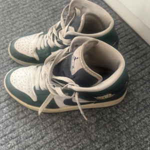 Nike Air Jordan 1 Mid grön/vit - Säljer ett par Nike Air Jordan 1 Mid sneakers i grön, vit och marinblå färg. Med snörning, perforerad och Air Jordan logga på sidan. I skinn och syntet. 