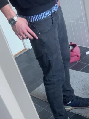 Svarta jeansbyxor med blått bälte - Snygga svarta jeansbyxor med klassisk femficksdesign. Byxorna har ett blåvitt mönstrat bälte som ger en cool kontrast. Perfekta för dig som gillar en enkel men stilren look. Passar till sneakers och hoodie.