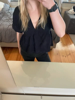 Svart blus med v-ringning från Lindex - Säljer en svart blus från Lindex i storlek S. Blusen har djup v-ringning, korta ärmar och en luftig, loose passform. Materialet är lätt och känns som bomull, perfekt för vår och sommar. Enkel och stilren design som funkar till många olika looks.