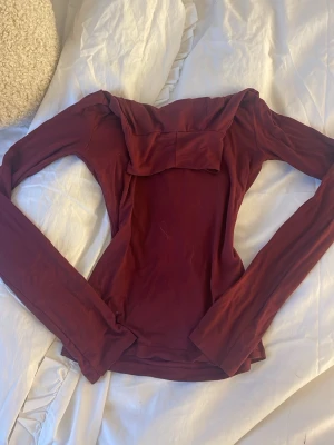 Vinröd långärmad topp från Gina Tricot - Säljer en vinröd långärmad topp från Gina Tricot i storlek XS. Toppen har en snygg omlottkrage som ger en cool detalj och är gjord i mjukt, stretchigt material som sitter slim på kroppen. Perfekt för dig som gillar stilrena plagg med lite edge.