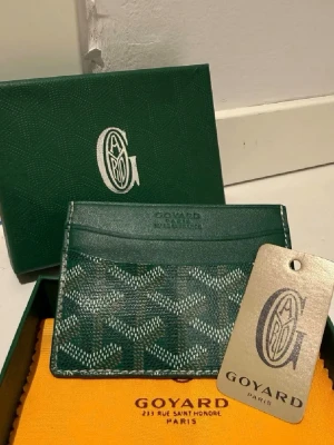 Plånbok  - Säljer en grön plånbok  med ikoniskt mönster och flera fack för kort.  Kommer med original ask och dustbag. Perfekt för dig som gillar exklusiva accessoarer.