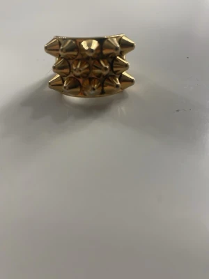 Edblad ring guld - Bilderna visar en guldfärgad ring med nitar, inte en väst. Ingen information om väst kan ges utifrån dessa bilder.