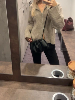 Milano svart clutchväska i skinn storlek small  - Säljer en stilren svart clutchväska från raffinato med mjukt skinnmaterial och snyggt rynkad design. Väskan har en axelrem som gör den enkel att bära crossbody och passar perfekt till olika outfits. Enkel och modern form som ger en cool vibe.