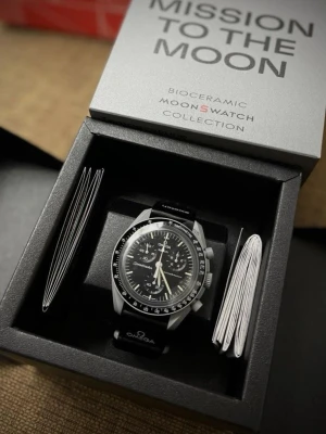 Omega x Swatch MoonSwatch Mission to the Moon - Omega x Swatch MoonSwatch Mission to the Moon, en stilren klocka med svart urtavla och grå boett. Klockan har tachymeter, kronograf och detaljerad måndesign på baksidan. Svart textilband med Omega och Swatch-logga. Perfekt för dig som gillar coola detaljer och ikonisk design.