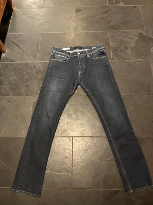 Replay Grover mörkblå jeans - Säljer ett par Replay Grover jeans i mörkblå tvätt med raka ben och snygga kontrastsömmar. Klassisk femficksmodell med Replay-logga på bakfickan och detaljerade sömmar. Jeansen är tillverkade i slitstarkt bomullsmaterial och har normal passform. Storlek W:34 L:32