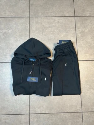 Svart Ralph lauren tracksuit - Svart Ralph lauren tracksuit med zip tröja samt medföljande byxor. Perfekt för chill-kalla dagar. Storlek large men är mer som M. Helt ny med tagg!