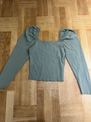 Grön långärmad topp  - Snygg grön långärmad topp från Dilvin med puffade axlar och fyrkantig halsringning. Stickad i mjukt material som ger en skön känsla. Perfekt att styla med jeans eller kjol för en trendig look.