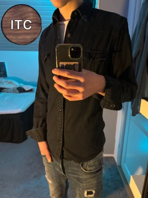 skjorta - Säljer en svart/mörblå skjorta från dressman med klassisk krage och bröstfickor. Skjortan har långa ärmar och stängs med knappar framtill. Perfekt till jeans för en avslappnad men snygg look.