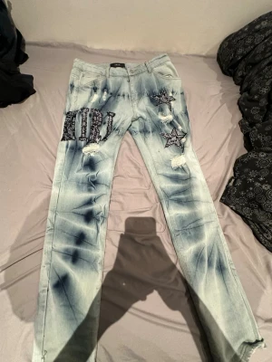 AMIRI ljusblå jeans med patchar - Säljer ett par sjukt snygga ljusblå jeans från AMIRI med coola batikdetaljer och svarta patchar i form av stjärnor och bokstäver. Jeansen har distressed detaljer och raka ben, samt silverfärgad knapp med AMIRI-logga. Perfekt för dig som vill sticka ut.