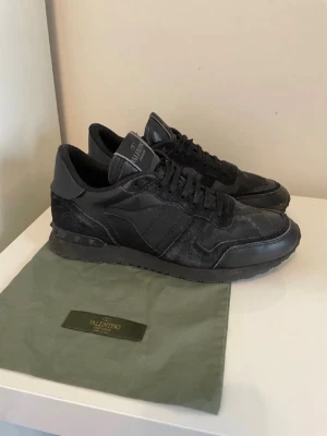 Valentino Garavani Rockrunner  - Svarta Valentino Garavani Rockrunner  med snygga detaljer i mocka och skinn. Skorna har snörning, rund tå och platt sula med mönstrad undersida.Perfekt för dig som gillar exklusiva sneakers och ett par schyssta skor nu i vinter. Str 40 men passar även 41.
