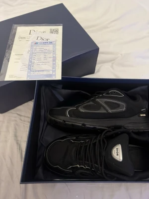 Svarta B30 sneakers - Säljer ett par svarta B30 sneakers med coola grå och silverdetaljer. Skorna har meshpaneler, snörning och en chunky platt sula. Märket syns tydligt på sidan och tungan. Perfekta för dig som vill ha en lyxig och modern sneaker med snygg design.