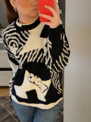 Svartvit stickad tröja Aelfric Eden - Unik svart och vit stickad tröja från Aelfric Eden med grafiskt mönster. Oversized fit med ribbade muddar och rund hals. Perfekt för dig som vill sticka ut och gillar streetwear-vibe.