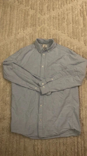 LJUSBLÅ SKJORTA  - Ljusblå skjorta från HM storlek S Regular. En liten defekt på nedre delen av ryggen, finns bild. Använd ett fåtal gånger.