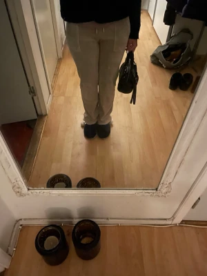 Beige mjukisbyxor från Juicy Couture - Säljer ett par beige mjukisbyxor från Juicy Couture med broderad logga på sidan. Byxorna har snörning i midjan och raka ben. Materialet är mjukt och skönt, perfekt för chill dagar. Färgen är ljusbeige och de har praktiska fickor framtill.