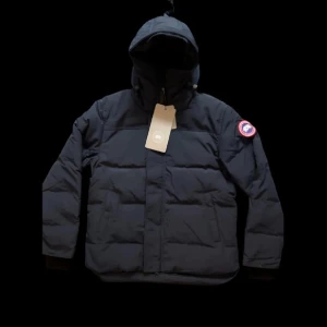 Canada Goose Jacka - Mörkblå pufferjacka från Canada Goose med huva och klassisk logotyp på vänster ärm. Jackan har quiltad design, dragkedja framtill och är långärmad. Perfekt för kalla dagar och har en clean, stilren look som funkar till allt. Storlek L men liten i storlek så passar även M och S. 